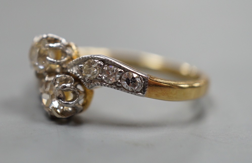 A yellow metal and two stone diamond set crossover ring, with diamond set shoulders, size J, gross weight 3.1 grams.